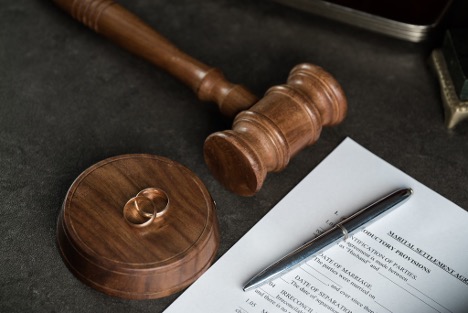 Wooden judge's gavel, wedding rings, and a marital settlement agreement document on a desk, representing divorce proceedings, family law matters, and legal agreements related to separation and child support.